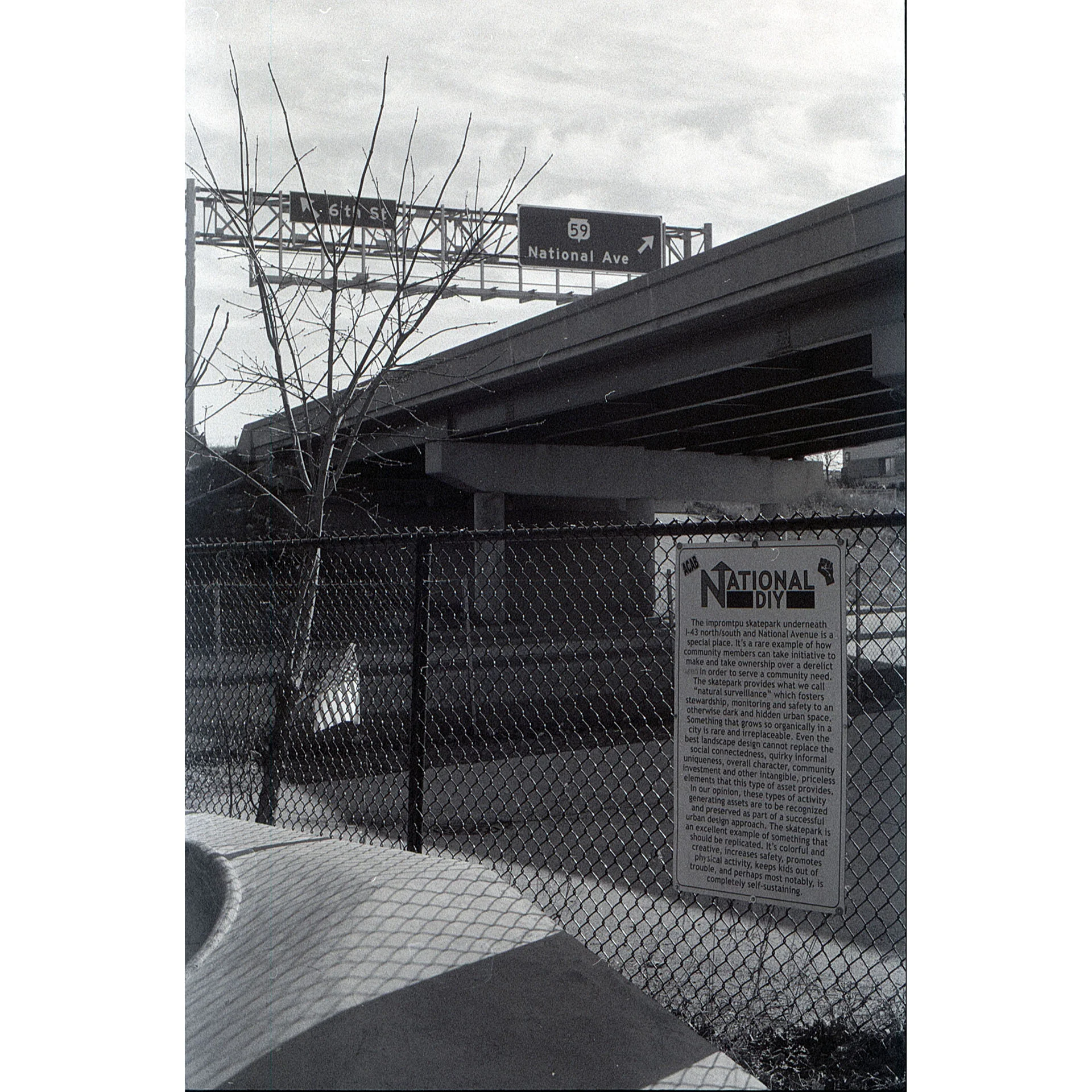 Black and white photo showing the old National DIY skatepark sign and the National Ave street sign in the background.
